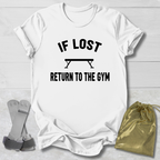 White t-shirt with 'If lost, return to the gym' text on a light wooden surface with socks and a drawstring bag.