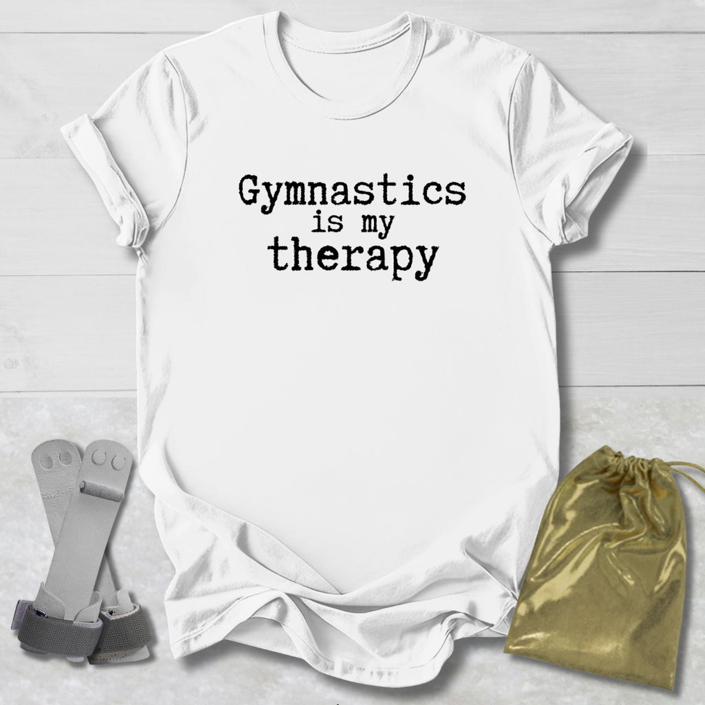 White t-shirt with 'Gymnastics is my therapy' text, socks, and drawstring bag on a light wooden surface.