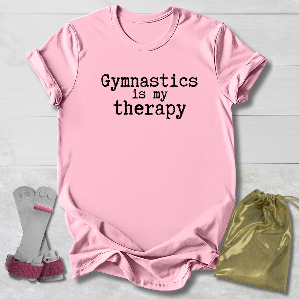 Pink t-shirt with 'Gymnastics is my therapy' text, socks, and drawstring bag on a light wooden surface.