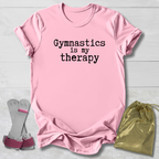 Pink t-shirt with 'Gymnastics is my therapy' text, socks, and drawstring bag on a light wooden surface.