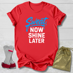 Red t-shirt with 'Sweat Now Shine Later' text, socks, and drawstring bag on a light wooden surface