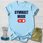 Light blue t-shirt with 'GYMNAST MODE ON' text, socks, and drawstring bag on a light wooden surface