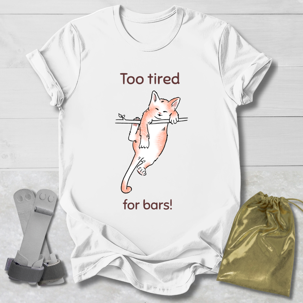White t-shirt with a cat graphic and text 'Too tired for bars!' on a wooden surface with socks and a drawstring bag.