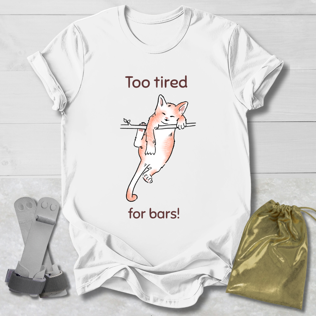 White t-shirt with a cat graphic and text 'Too tired for bars!' on a wooden surface with socks and a drawstring bag.