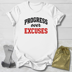 White t-shirt with 'PROGRESS over EXCUSES' text on a light wooden surface with socks and a drawstring bag.