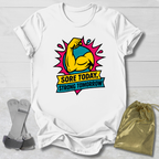 White t-shirt with a colorful graphic and text 'Sore Today, Strong Tomorrow' on a light wooden surface.