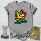 Gray t-shirt with a colorful graphic and text 'Sore Today, Strong Tomorrow' on a light wooden surface.