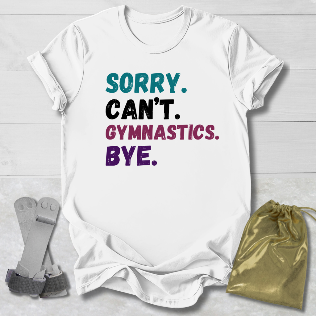 White t-shirt with colorful text 'Sorry. Can't. Gymnastics. Bye.' on a light wooden surface.