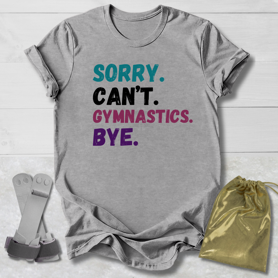 Gray t-shirt with colorful text 'Sorry. Can't. Gymnastics. Bye.' on a wooden surface with socks and a drawstring bag.