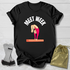 Black t-shirt with gymnastics graphic and text on a light wooden surface with socks and a drawstring bag.