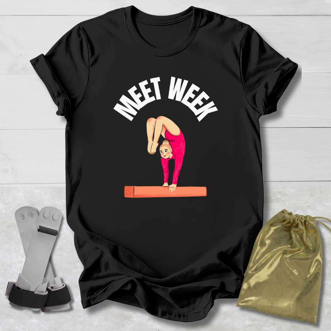 Black t-shirt with gymnastics graphic and text on a light wooden surface with socks and a drawstring bag.