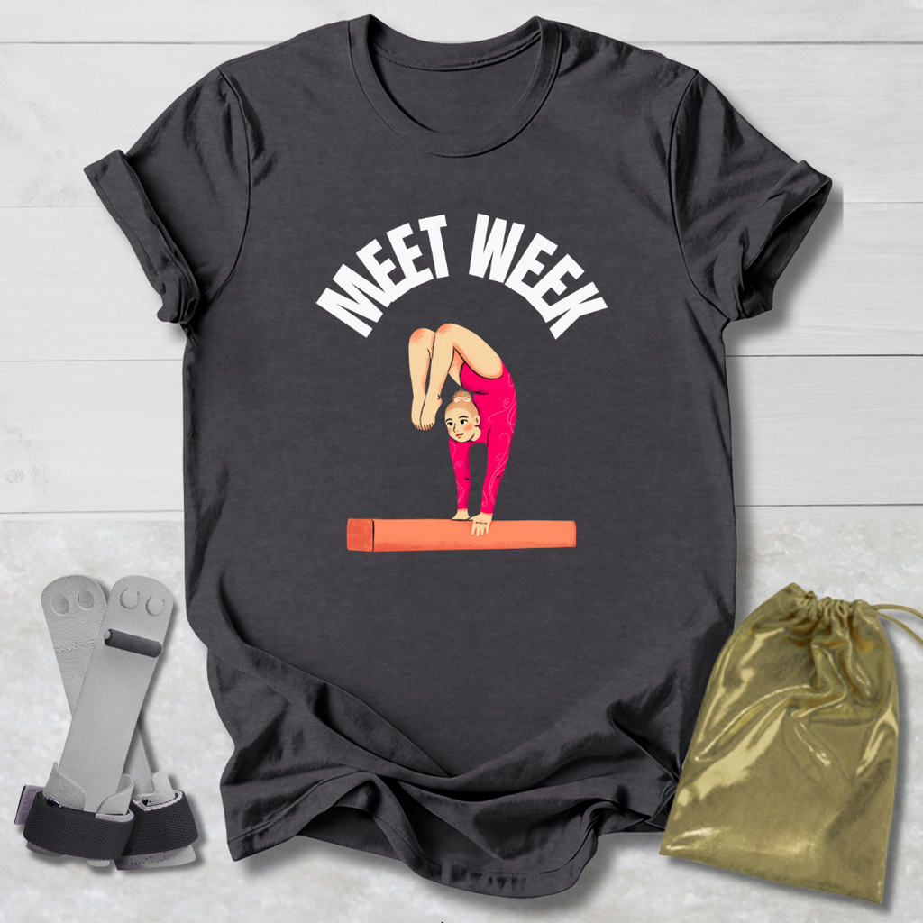 Black t-shirt with a graphic of a gymnast on a balance beam and text 'MEET WEEK' on a wooden surface.