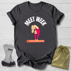 Black t-shirt with a graphic of a gymnast on a balance beam and text 'MEET WEEK' on a wooden surface.