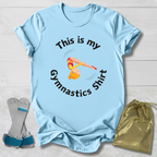 Light blue t-shirt with gymnastics-themed text and graphics, accompanied by socks and a drawstring bag on a light wooden surface.