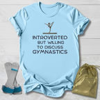 Light blue t-shirt with gymnastics-themed text and graphics on a wooden surface.