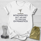 White t-shirt with gymnastics-themed text and graphics on a light wooden surface.