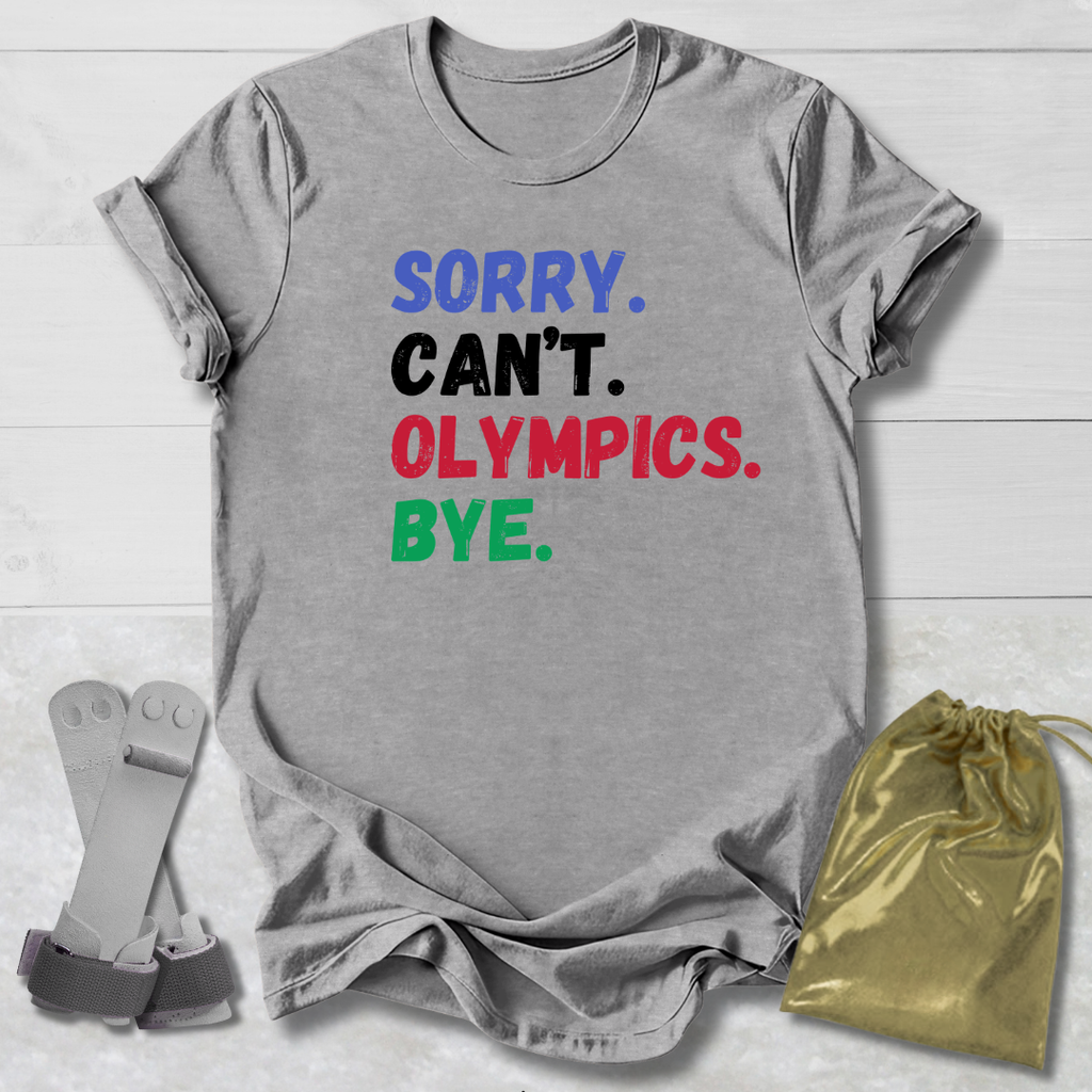Gray t-shirt with colorful text 'SORRY. CAN'T. OLYMPICS. BYE.' on a light wooden surface.