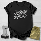 Black t-shirt with 'I probably need glitter' text on a light wooden surface with socks and a drawstring bag.