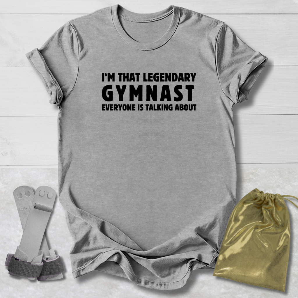 Gray t-shirt with text 'I'm that legendary gymnast everyone is talking about' on a wooden surface with socks and a drawstring bag.