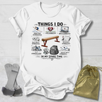 White t-shirt with a gymnastics things I do graphic design on a wooden surface with socks and a drawstring bag.