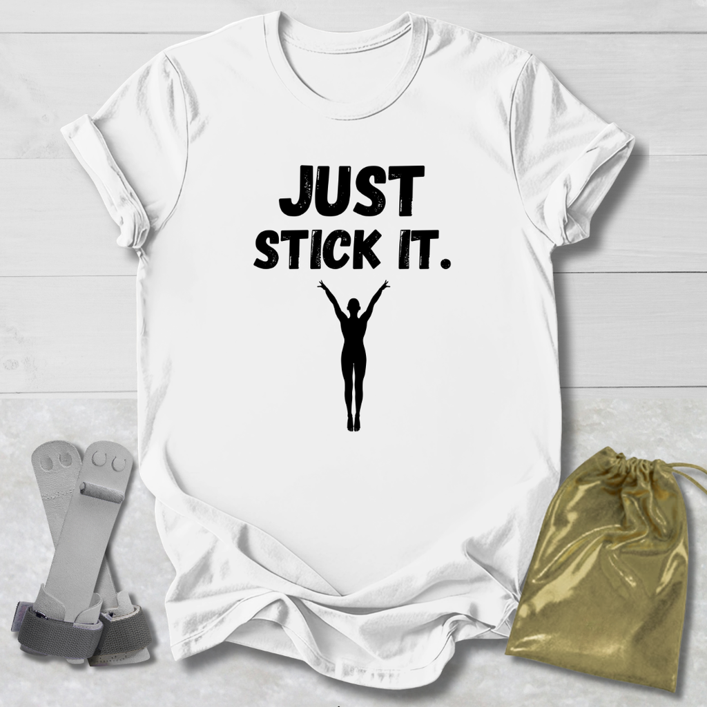 White gymnastics gymnast t-shirt with 'JUST STICK IT.' text and silhouette graphic on a light wooden surface.