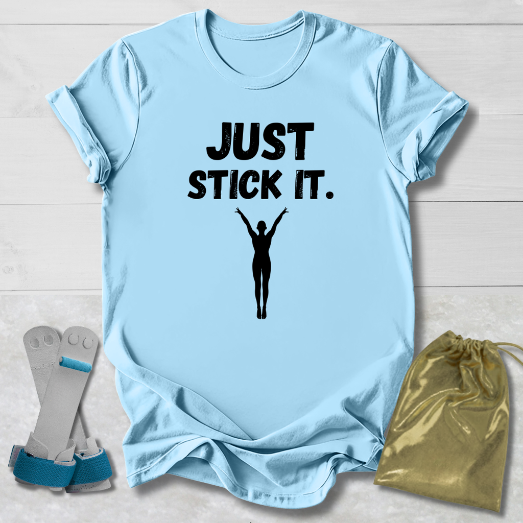 Light blue gymnastics gymnast t-shirt with 'JUST STICK IT.' text and silhouette, socks, and drawstring bag on a light wooden surface.