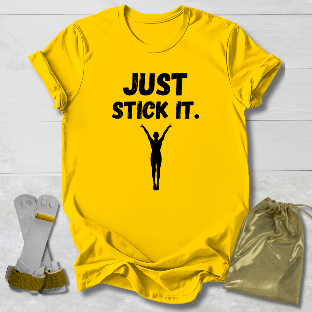 Yellow gymnastics gymnast t-shirt with 'JUST STICK IT.' text and silhouette, socks, and drawstring bag on a light wooden surface.