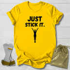 Yellow gymnastics gymnast t-shirt with 'JUST STICK IT.' text and silhouette, socks, and drawstring bag on a light wooden surface.