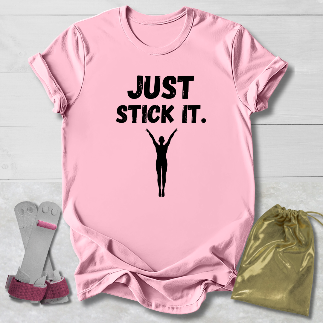 Pink gymnastics gymnast t-shirt with 'JUST STICK IT.' text and silhouette, socks, and drawstring bag on a light wooden surface.
