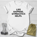 White t-shirt with 'Life happens. Gymnastics helps.' text, socks, and drawstring bag on a light wooden surface.