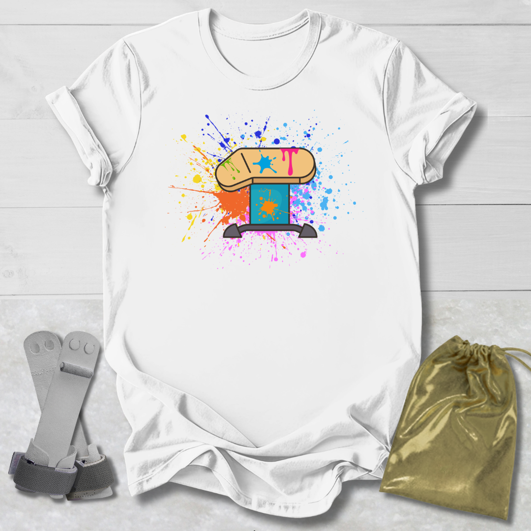 White t-shirt with colorful graphic design on a light wooden surface, accompanied by gray socks and a gold drawstring bag.
