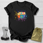 Black t-shirt with colorful graphic design on a light wooden surface, with socks and a drawstring bag in the foreground.