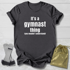 Maroon t-shirt with 'It's a gymnast thing (you wouldn't understand)' text, socks, and drawstring bag on a light wooden surface.