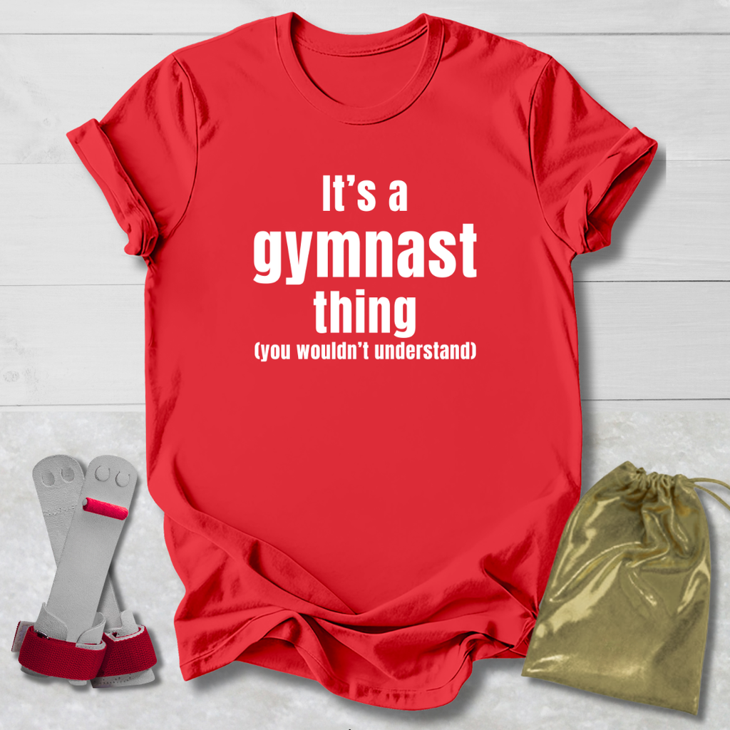 Red t-shirt with 'It's a gymnast thing (you wouldn't understand)' text, socks, and drawstring bag on a light wooden surface.