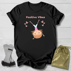 Black t-shirt with 'Positive Vibes' text and cartoon design on a wooden surface with socks and a drawstring bag.