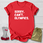 Red t-shirt with 'SORRY. CAN'T. OLYMPICS.' text, socks, and drawstring bag on a light wooden surface.