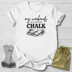 White t-shirt with 'my weekends are covered in CHALK' text and graphic on a light wooden surface.
