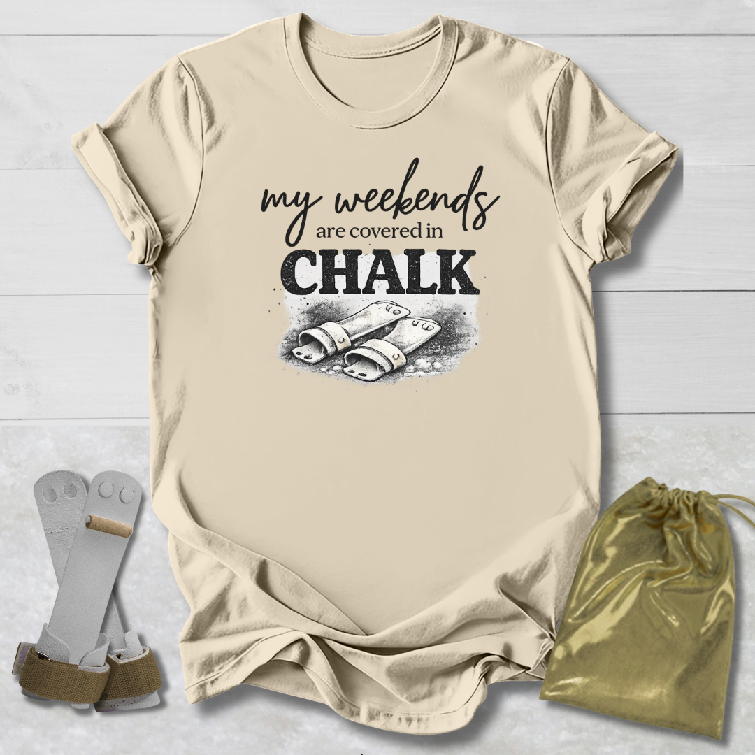 Beige t-shirt with 'my weekends are covered in CHALK' text and graphic, socks, and drawstring bag on a light wooden surface.
