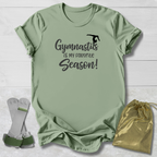 Green t-shirt with 'Gymnastics is my favorite season!' text, socks, and drawstring bag on a light wooden surface.