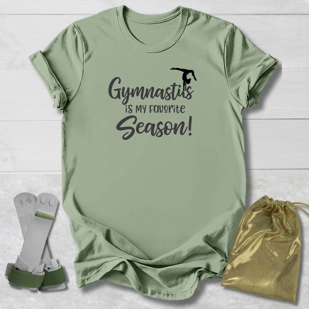 Green t-shirt with 'Gymnastics is my favorite season!' text, socks, and drawstring bag on a light wooden surface.