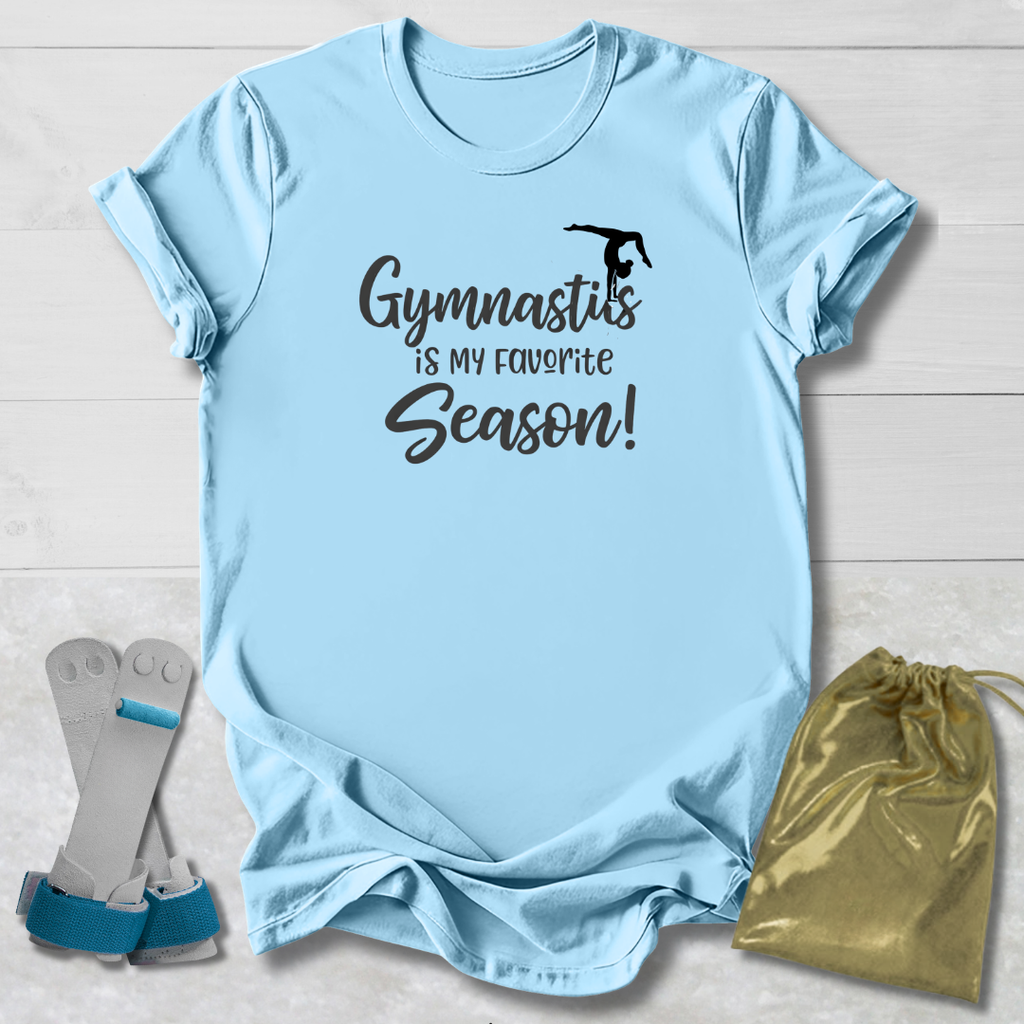 Light blue t-shirt with 'Gymnastics is my favorite season!' text, socks, and drawstring bag on a wooden surface.