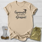 Beige t-shirt with 'Gymnastics is my favorite season!' text, socks, and drawstring bag on a light wooden surface.