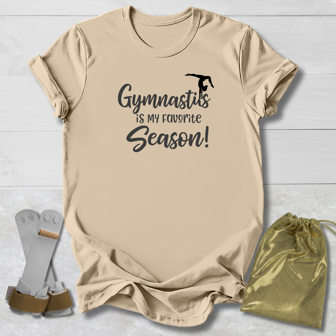 Beige t-shirt with 'Gymnastics is my favorite season!' text, socks, and drawstring bag on a light wooden surface.