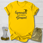 Yellow t-shirt with 'Gymnastics is my favorite season!' text, socks, and drawstring bag on a light wooden surface.