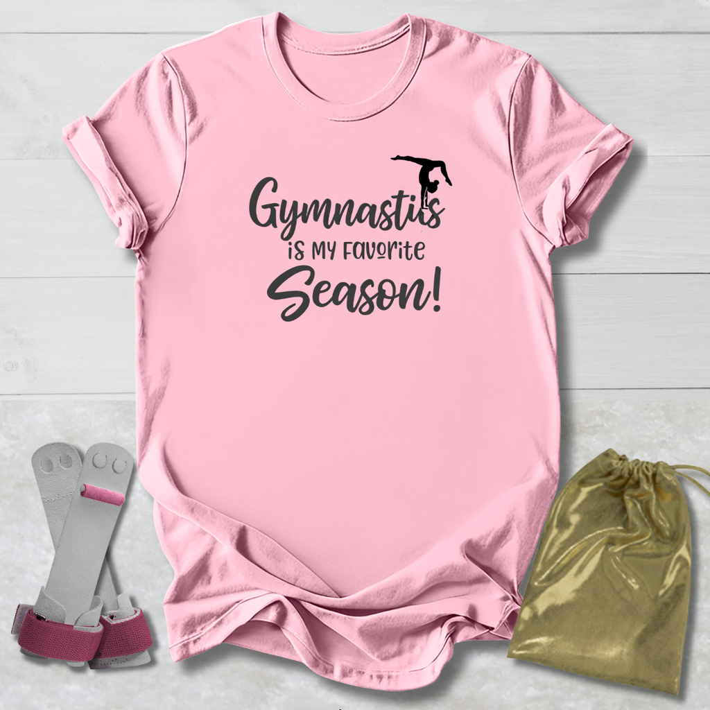 Pink t-shirt with 'Gymnastics is my favorite season!' text, socks, and drawstring bag on a light wooden surface.
