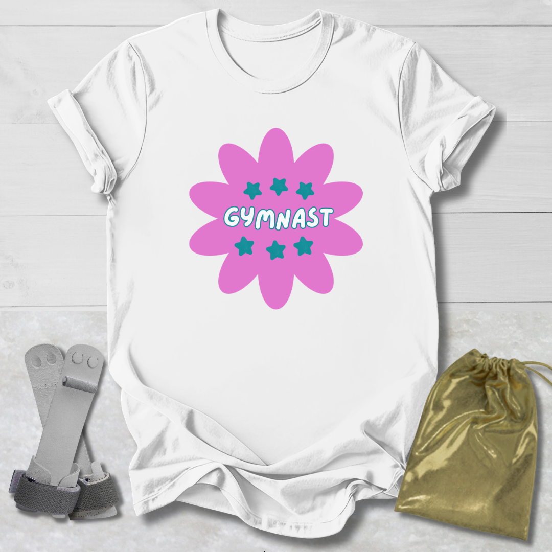 White t-shirt with a pink floral design and 'GYMNAST' text, placed on a light wooden surface with socks and a drawstring bag.