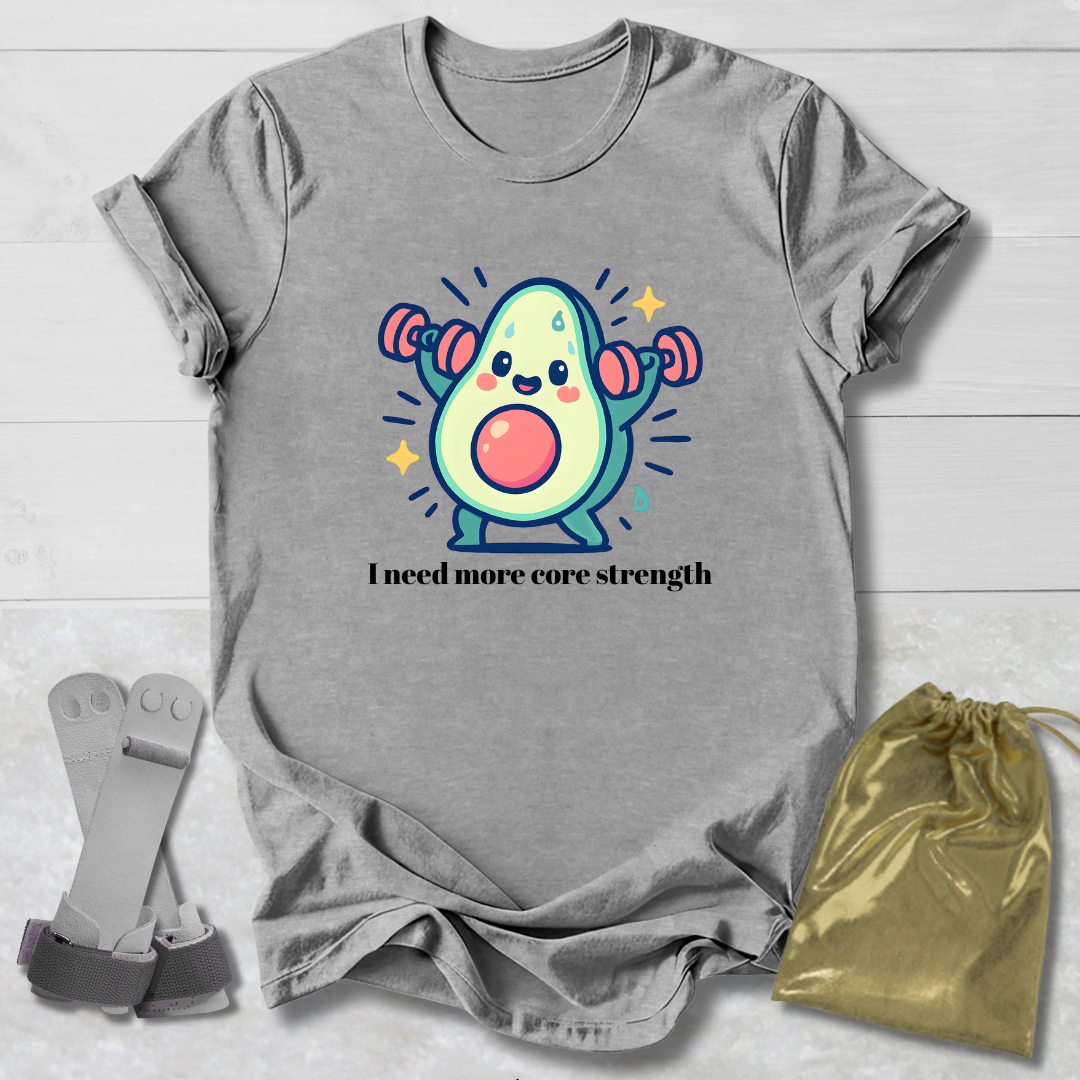 Gray t-shirt with a cartoon avocado lifting weights and text 'I need more core strength' on a wooden surface.