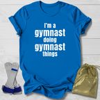 Blue t-shirt with 'I'm a gymnast doing gymnast things' text and drawstring bag on a light wooden surface.