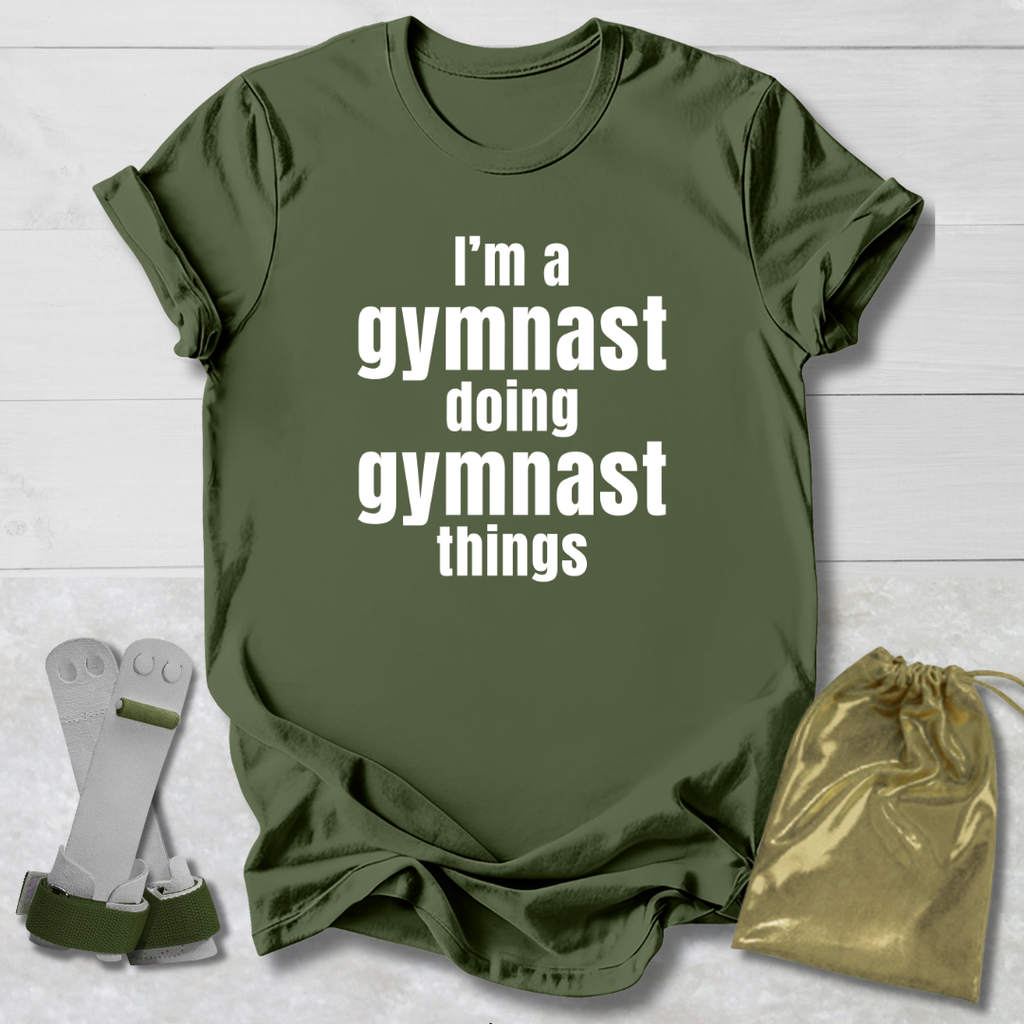 Green t-shirt with 'I'm a gymnast doing gymnast things' text, socks, and drawstring bag on a light wooden surface.