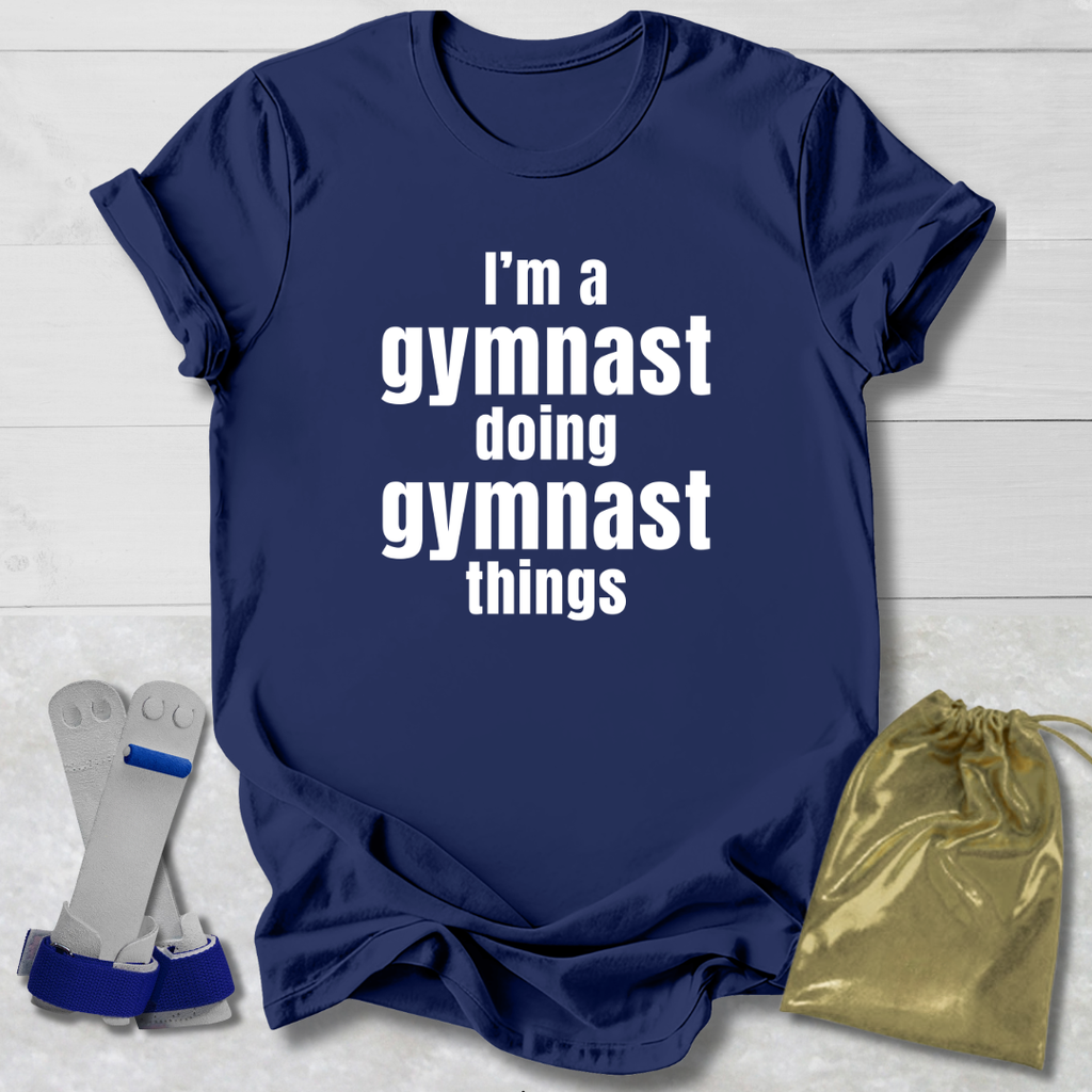 Navy blue t-shirt with 'I'm a gymnast doing gymnast things' text, socks, and drawstring bag on a light wooden surface.